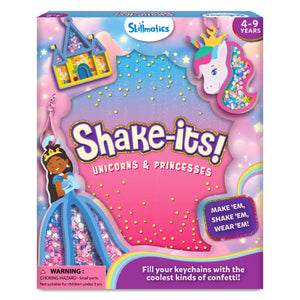 Front view of the Skillmatics “Shake-its! Unicorns & Princesses” activity kit box with a pastel pink, purple, and blue sky background. The packaging features foam shake-it designs including a unicorn head, a princess in a blue gown, and a castle, each filled with colorful confetti. Visible text includes the Skillmatics logo, age range 4–9 years, a “Make ’em, shake ’em, wear ’em” callout, and a small choking hazard warning.