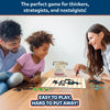 A family of three — a father, mother, and child — sitting around a wooden table, playing the Skillmatics Boxed! game. The game board is on the table, with the family placing magnetic pieces and dots. The child is smiling and making a move while the parents watch with interest. The cloth bag with the Boxed! logo is placed beside them, and the tagline