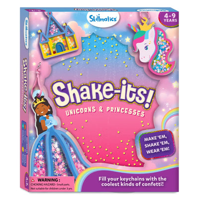 Front view of the Skillmatics “Shake-its! Unicorns & Princesses” activity kit box with a pastel sky background of clouds, stars, and sparkles. Illustrated foam shake-its include a unicorn head, a princess in a blue gown, and a castle filled with confetti. Visible elements include the Skillmatics logo, age range 4–9 years, a “Make ’em, shake ’em, wear ’em” badge, a rainbow graphic, and a choking hazard warning.