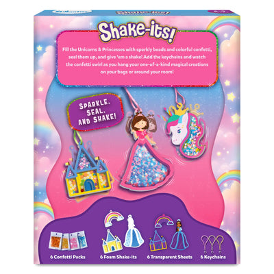Back view of the Shake-its Unicorns & Princesses packaging showing hanging finished shake-it keychains, including a princess, unicorn, and castle, each filled with confetti and shown mid-swirl. A pink text panel explains the activity steps, while a purple section at the bottom displays icons and labels for contents: six confetti packs, six foam shake-its, six transparent sheets, and six keychains, set against a rainbow and cloud background.