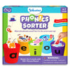Skillmatics Phonics Sorter educational game box for ages 4 to 7, featuring five colorful cups labeled a, e, i, o, and u. Illustrated picture pieces like cat, bed, pig, jam, hat, and cup are shown being sorted into vowel cups. The box highlights phonemic awareness, speech and listening skills, includes 100 plus picture pieces, shows hands-on play, and displays a child-friendly, bright learning design.