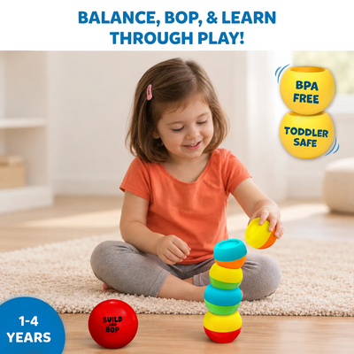 A toddler sits on a soft rug indoors, balancing colourful wobbly pieces from the Build And Bop toy while a red ball labeled “Build And Bop” sits nearby. Text at the top reads “Balance, bop, & learn through play!”. Two yellow icons on the right state “BPA Free” and “Toddler Safe,” and a blue badge on the bottom left indicates the toy is for ages 1–4 years.