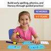 Smiling young girl seated at a table practicing spelling on blue write-and-wipe cards using a dry-erase marker. Visible word cards include simple phonics words, with another marker and cloth placed nearby. Text reads “Build early spelling, phonics, and literacy through guided practice,” alongside badges for 90 words and ages 4–7.