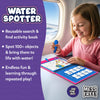 A young child seated by an airplane window happily using the Skillmatics Water Spotter activity book on a tray table, holding a blue refillable water pen to reveal colorful hidden objects. The open book shows search and find pages with illustrations. Text highlights reusable play, spotting 100+ objects, mess-free fun, and portability for travel and on-the-go learning.