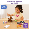 Young child wearing the included pink stethoscope examines the plush puppy using tweezers while playing with the Skillmatics Vet Set. The table displays X-ray sheets, flea spray, medicine, prescription pad, syringe, ointment tube, felt ticks, and other pretend veterinary tools for ages 3–8.