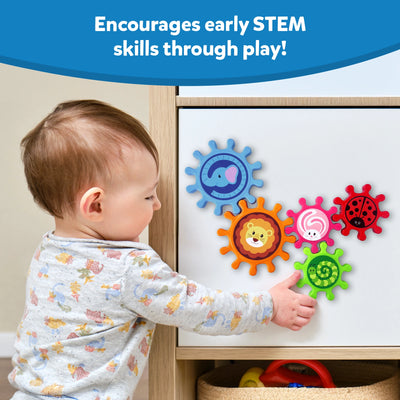 A toddler in patterned pajamas plays with the Skillmatics Spinny Gears toy on a cabinet surface. The colourful gears interlock and spin, each featuring a different animal. The caption reads “Encourages early STEM skills through play!” highlighting how the toy promotes cause-and-effect learning, hand-eye coordination, and sensory exploration.
