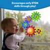 A smiling baby stands by a glass window playing with Skillmatics Spinny Gears Pattern Pop toy. The colourful suction gears—featuring bold swirl, stripe, and spiral designs—stick to the glass and spin when moved. The caption reads “Encourages early STEM skills through play!” showcasing how the sensory toy helps develop curiosity, fine motor skills, and problem-solving abilities.