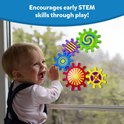 A smiling baby stands by a glass window playing with Skillmatics Spinny Gears Pattern Pop toy. The colourful suction gears—featuring bold swirl, stripe, and spiral designs—stick to the glass and spin when moved. The caption reads “Encourages early STEM skills through play!” showcasing how the sensory toy helps develop curiosity, fine motor skills, and problem-solving abilities.