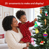 A child and parent decorating a Christmas tree together using Skillmatics Foil Fun ornaments. The child smiles while hanging colourful handmade foil decorations, including stars, stockings, snowmen and baubles, creating a festive family activity scene in a bright home setting.