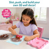 Young girl sitting at a table engaging with Skillmatics Stixels 3D art kit, carefully inserting colored stixel pegs into a transparent base using a color guide. The scene shows a pastel pink creative workspace with finished puppy design forming, bowls of stixels, and a calm, focused play activity.