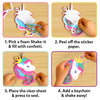 A four-panel instructional layout shows hands assembling a unicorn foam shake-it on a wooden surface. Steps include filling sections with colorful confetti, peeling off white backing paper, placing a transparent sheet to seal the foam shape, and attaching a keychain loop through the top hole. Each step is numbered and framed against a purple background for clear visual guidance.