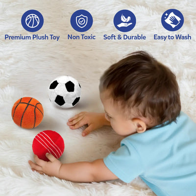 Baby lying on a soft white textured surface reaches toward three plush sports balls placed nearby: an orange basketball, a black-and-white soccer ball, and a red cricket ball with stitched lines. At the top, four blue circular icons with labels read Premium Plush Toy, Non Toxic, Soft & Durable, and Easy to Wash, highlighting key material and care features.