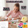 Girl with ponytail coloring a nature stencil using Skillmatics magic iron-on markers at a wooden desk. Printed design sheets, multiple colorful markers visible. Finished items shown: yellow cap with pineapple iron-on and canvas tote with colorful flower designs. Text: Make It. Iron It. Own It.