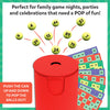 Close-up illustration of the Pop-Reveal Housie game setup. A red pop-reveal can releases multiple yellow numbered balls upward, with colorful reusable housie cards fanned behind it. The headline reads “Housie made dynamic, with a POP!” Emphasis is placed on the popping action, number visibility, and reusable card design.