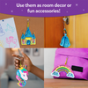 A collage shows finished shake-it keychains used in everyday settings. A castle shake-it hangs on a corkboard near children’s drawings, a princess shake-it hangs from a door handle, a unicorn shake-it is held in a child’s hand, and a rainbow shake-it is clipped to a pink backpack. Text above reads “Use them as room decor or fun accessories!”