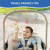 Baby seated in a padded stroller reaches upward to touch colorful plastic Linkies hanging from the stroller handle. The links in yellow, green, blue, orange, and red are clipped individually and in short chains. A blue banner at the top reads “Travel-Friendly Toy.” The background shows a softly blurred outdoor path, emphasizing on-the-go play and reach-and-grasp interaction.