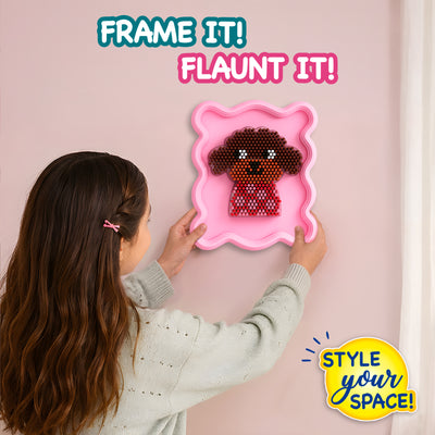 Young girl seen from behind carefully holds a pink wavy frame mounted on a wall, showcasing a completed 3D puppy design made with Stixels pegs. Bold text reads ‘FRAME IT! FLAUNT IT!’ and ‘STYLE YOUR SPACE!’, highlighting DIY wall décor in a soft pastel interior setting.