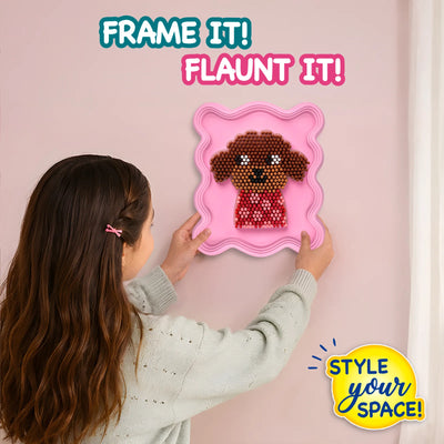 Young girl seen from behind carefully holds a pink wavy frame mounted on a wall, showcasing a completed 3D puppy design made with Stixels pegs. Bold text reads ‘FRAME IT! FLAUNT IT!’ and ‘STYLE YOUR SPACE!’, highlighting DIY wall décor in a soft pastel interior setting.