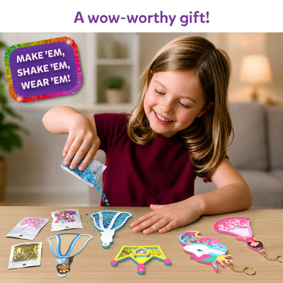 A smiling child sits at a table pouring blue confetti from a small packet into a unicorn-shaped foam shake-it. On the tabletop are additional foam shapes, transparent sheets, keychain loops, and multiple confetti packs in pink, gold, and multicolor. A purple badge reads “Make ’em, shake ’em, wear ’em,” while text above says “Fill your keychains with the coolest kinds of confetti.”