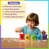 A young child smiling while sorting illustrated picture pieces into five colorful cups labeled a, e, i, o, and u placed on a wooden table. A highlighted panel titled “Teaches” lists phonemic awareness, vowel recognition, letter sound association, decoding skills, and auditory discrimination. Numerous picture tokens are scattered on the table, visually demonstrating hands-on phonics learning through vowel sound sorting.