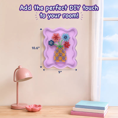 Skillmatics Stixels Flower Vase wall décor displayed in a room above a wooden desk with a pink lamp, decorative dish, stacked books, and a window. Measurement indicators show the framed artwork size as 10.6 inches tall by 9 inches wide, highlighting its suitability as DIY room decoration.