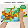 A hand interacting with the 'Whose Tail is That?' sensory cloth book, turning the pages that feature a tiger with a striped tail and a crocodile. The page has crinkly fabric sections, enhancing sensory interaction for the child. The plush tails of various animals, like a monkey and zebra, are attached to the book for tactile engagement, promoting early learning and sensory development.