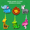 Six completed animal-shaped foam keychains are displayed on a green background with sparkle accents. The designs include an elephant, lion, zebra, giraffe, crocodile, and flamingo, each filled with colorful confetti and attached to a loop or clip. Text at the top reads “Make shake-its that sparkle & swirl!” with decorative leaves and light reflections around each figure.