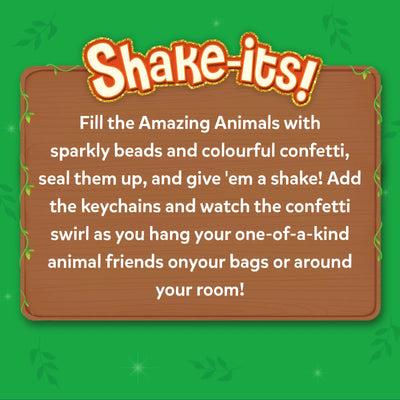 A wooden signboard graphic appears on a green jungle-themed background with leafy accents and sparkles. The heading reads “Shake-its!” followed by instructional text explaining how to fill animal shapes with sparkly beads and colorful confetti, seal them, shake them, and attach keychains. The layout resembles a playful notice board framed with vines and decorative stars.