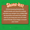 A wooden signboard graphic appears on a green jungle-themed background with leafy accents and sparkles. The heading reads “Shake-its!” followed by instructional text explaining how to fill animal shapes with sparkly beads and colorful confetti, seal them, shake them, and attach keychains. The layout resembles a playful notice board framed with vines and decorative stars.