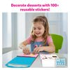 Young girl happily decorating desserts with reusable stickers from Peelies Dessert Chef activity book