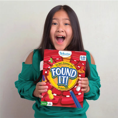 Girl holding a red Found It Board Game for ages 6 to 99, ready for fun scavenger hunts